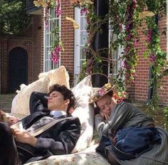 two people are laying on a couch with flowers hanging from the ceiling and one person is reading