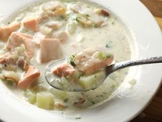 a white bowl filled with soup and meat on top of a wooden table next to a spoon