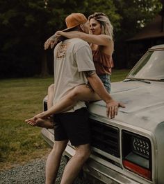 a man and woman leaning on the hood of a pickup truck while they are kissing