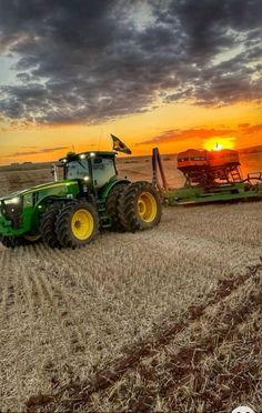 a tractor is driving in the middle of a field at sunset with a trailer behind it