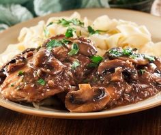 a close up of a plate of food with meat and mushrooms on it next to pasta