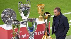 a man standing next to several trophies on top of a soccer field with grass in the background