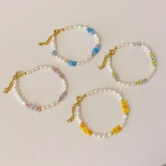 three bracelets with beads and charms on them sitting on a white surface, one is gold