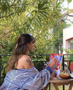 a woman sitting at a table painting outside