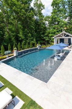 an outdoor pool with lounge chairs and umbrellas next to it, surrounded by trees