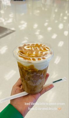 a hand holding a cup of iced coffee with caramel swirl on top and whipped cream in the bottom