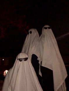 two people dressed in white are standing outside at night with their eyes covered by ghost costumes