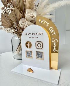 a white and gold stand with two earrings on it, next to a vase filled with flowers