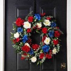 a wreath with red, white and blue flowers is on the front door of a house