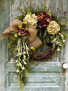 a wreath is hanging on the front door of an old wooden door with flowers and foliage