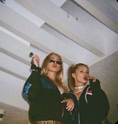 two women standing next to each other in front of a ceiling with lights on it