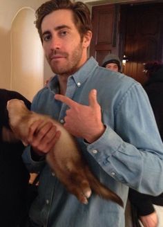 a man holding a cat in his right hand and giving the thumbs up sign to someone