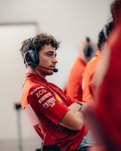 a man with headphones on standing in front of other men wearing red shirts and orange vests