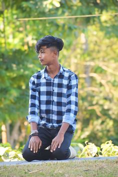 a young man sitting on the ground in front of trees