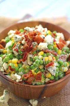 a wooden bowl filled with peas, bacon, and cheese on top of a table