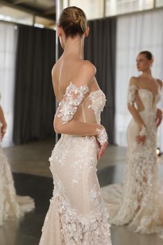 a woman in a wedding dress is looking at another woman wearing a gown with flowers on it