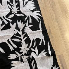 a black and white quilt with birds on it sitting on a wooden floor next to a wood floor