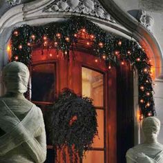 two statues are standing in front of a door decorated with lights and wreaths for the holiday season