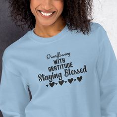 a woman wearing a light blue sweatshirt with black lettering on the front that says, questioning with gratitude staying blessed