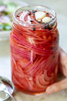 a jar filled with sliced red onions on top of a table next to a spoon