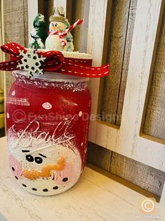 a painted jar sitting on top of a table next to a wooden fence with snowmen