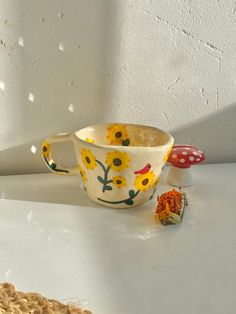 a cup with flowers painted on it next to a mushroom