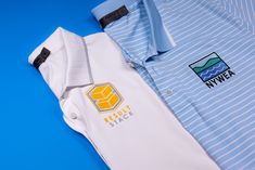 two polo shirts sitting next to each other on top of a blue surface with white and yellow stripes