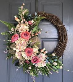 a wreath with pink flowers and greenery hangs on the front door's gray door