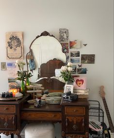 a desk with a mirror, flowers and other items on it in front of a white wall