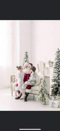 two children are sitting on a couch near christmas trees