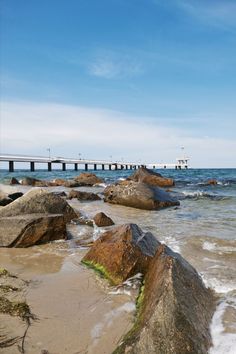 the beach is full of rocks and water with a pier in the backgroud