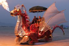 a dragon float on the beach with people sitting in it and an umbrella over its head