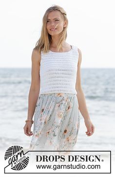 a woman standing on top of a beach next to the ocean wearing a white tank top