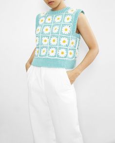 a woman is wearing white pants and a blue sweater with daisies on it,