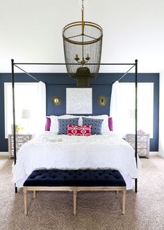 a bedroom with blue walls, white bedding and a birdcage hanging from the ceiling