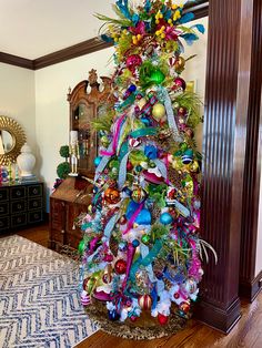 a brightly colored christmas tree in the corner of a room with an ornate mirror behind it