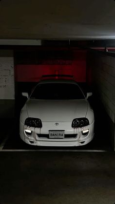 a white car parked in a parking garage with its hood up and the lights on