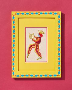 a cross stitch picture frame with a colorful bird on it's back and a red background