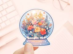 a person holding up a snow globe with flowers in it on top of a desk