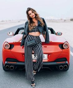 a woman sitting on top of a red sports car in the middle of an empty road