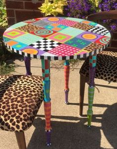 an animal print table and two chairs with colorful paint on the legs, sitting in front of a brick wall