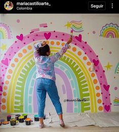 a woman painting a rainbow mural on the wall