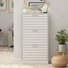 a white chest of drawers next to a potted plant in a room with pictures on the wall