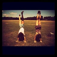 two people doing handstands in the middle of a field with their feet up