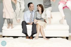 a man and woman sitting on a white couch with their children in the air above them