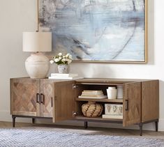 a living room with a painting on the wall next to a wooden cabinet and lamp