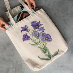 a person holding a tote bag with purple flowers painted on the front and side