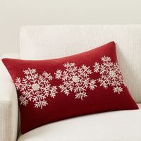 a red and white pillow with snowflakes on it sitting on a couch next to a chair