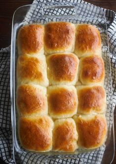 a glass baking dish filled with rolls on top of a checkered cloth next to a wooden table