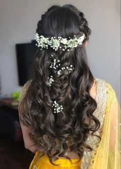 a woman with long dark hair wearing a yellow dress and flowers in her hair is seen from the back